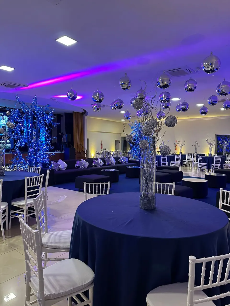Salão decorado em azul, com mesas redondas e cadeiras brancas
