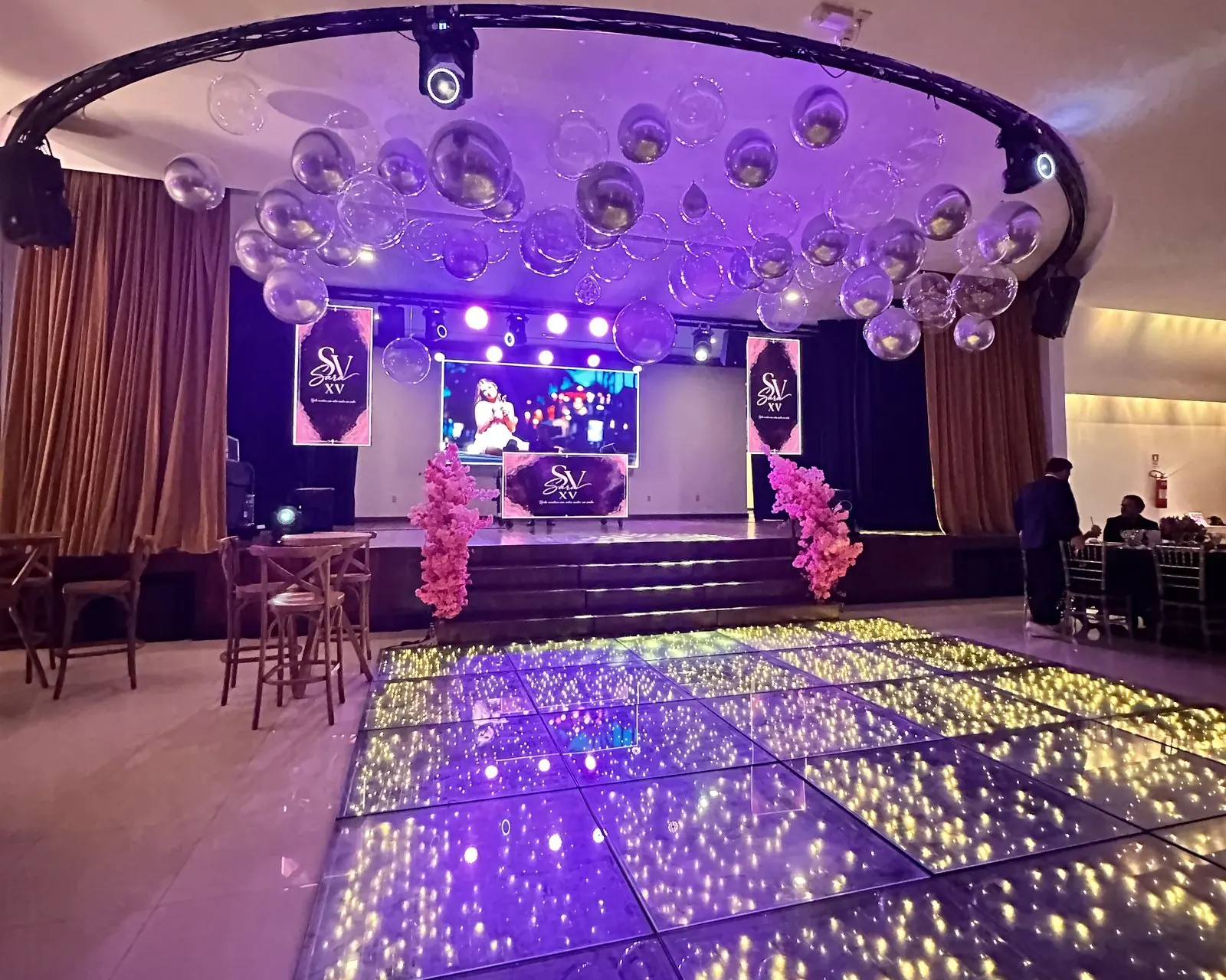 Salão Social montado para uma festa de 15 anos: palco com telão, pista de LED e balões no teto
